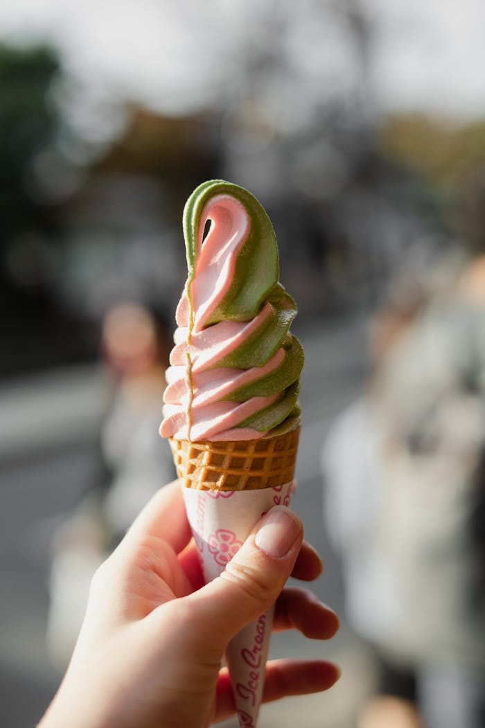 A hand holding swirled matcha and strawberry ice cream cone on a sunny day in Kyoto, Japan.