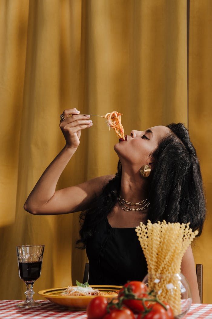 Stylish woman savoring spaghetti with red wine at a dining table.